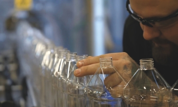 Flaskor står uppradade vid Rekals produktionsled för rengöringsprodukter och granskas av en man med skyddsglasögon. 
